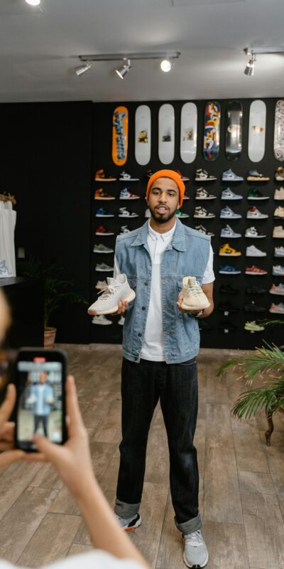 A man demonstrates shoes for an online promotional video in a boutique shop setting.